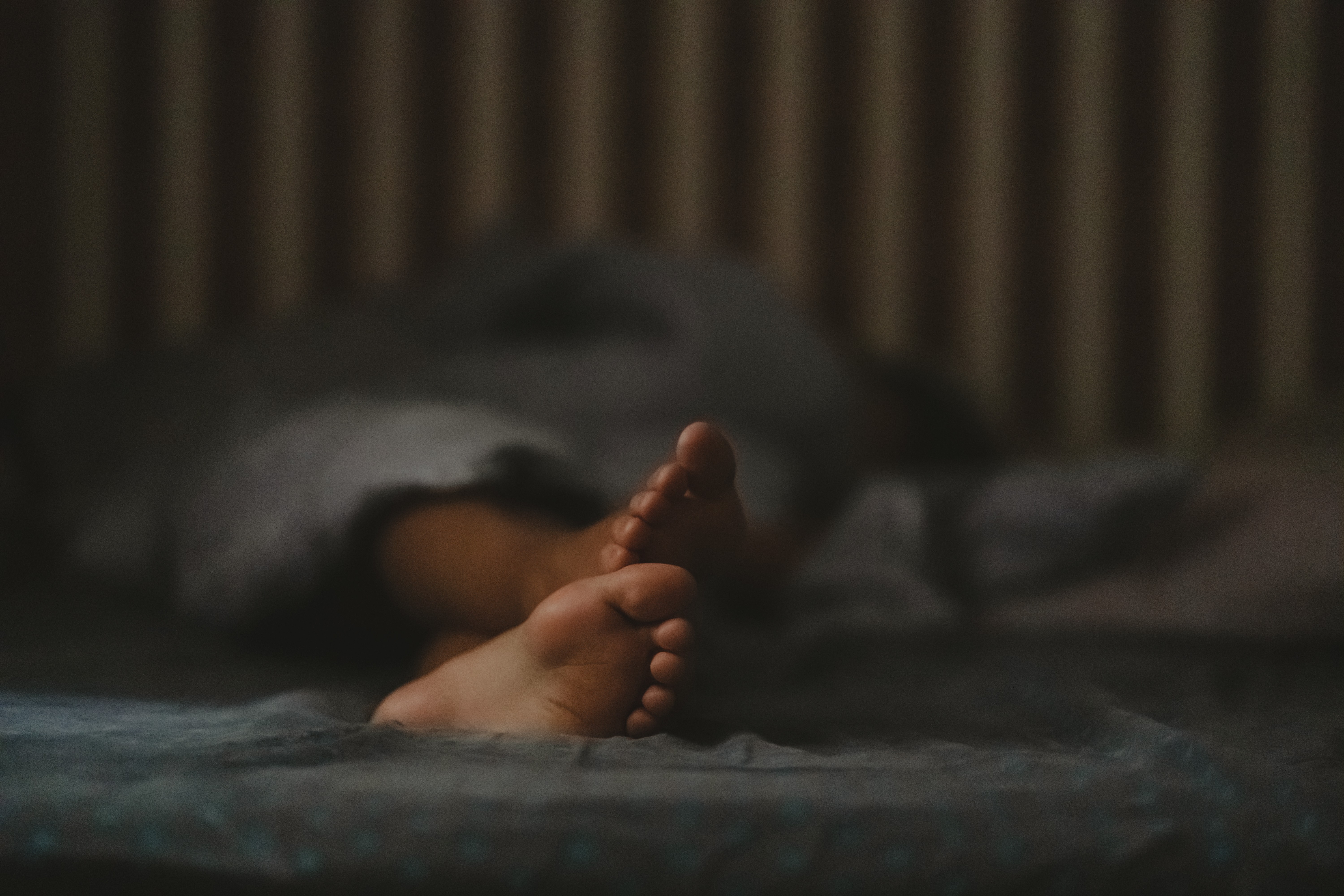 Feet protruding from bedding in a dark room. 