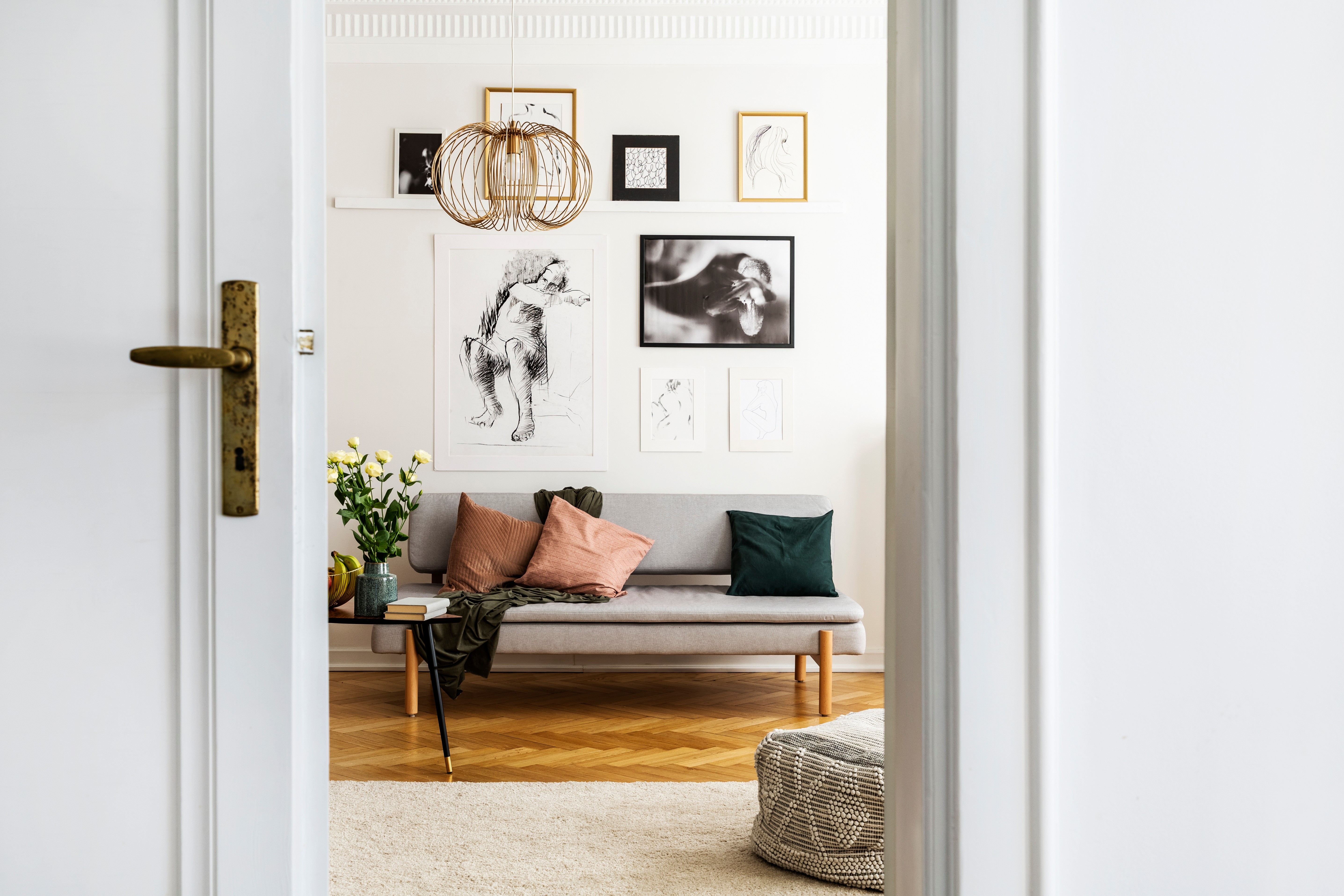 Door opening to room with mixed art gallery wall above gray sofa