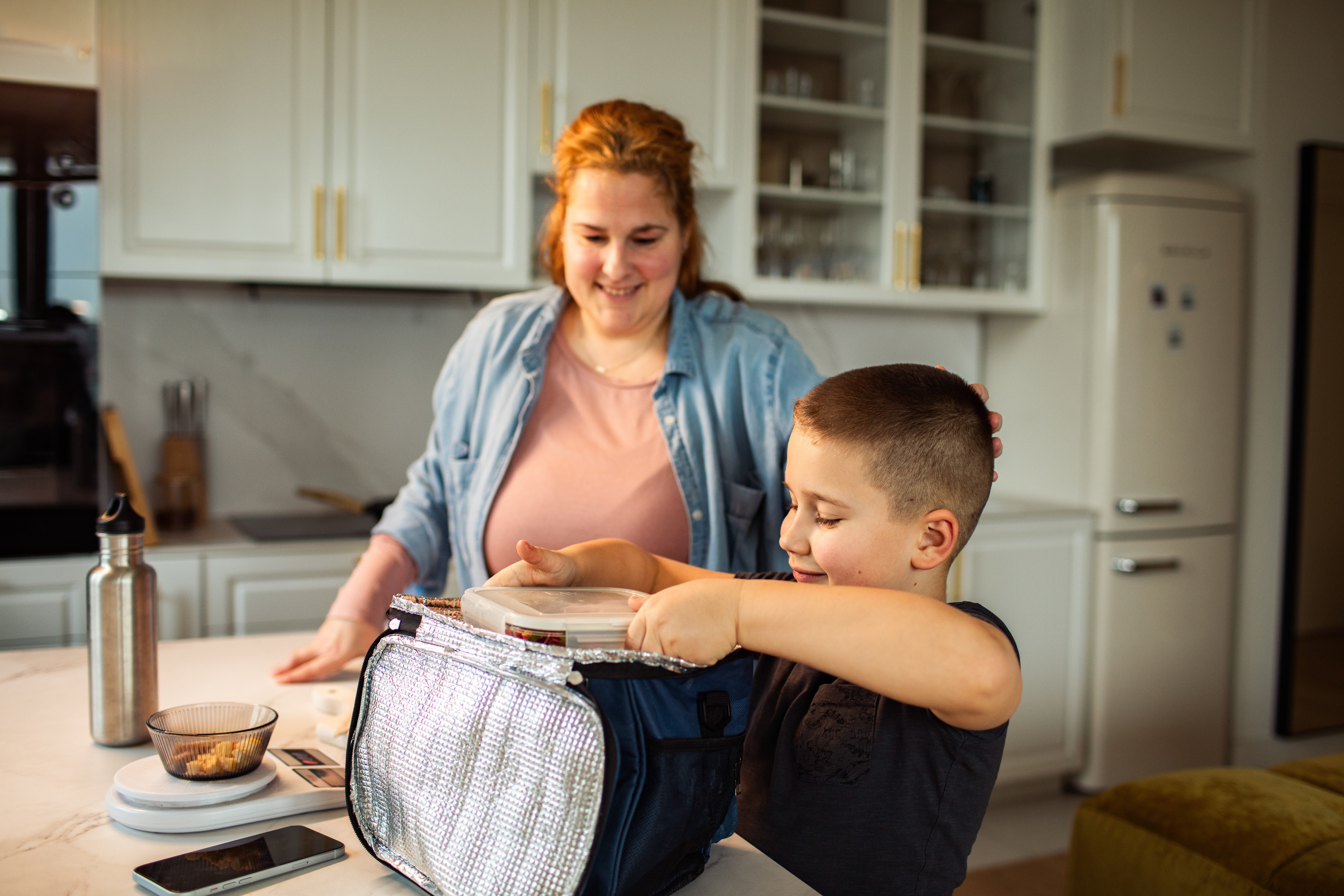 mom supervising son packing his own lunch in the kitchen