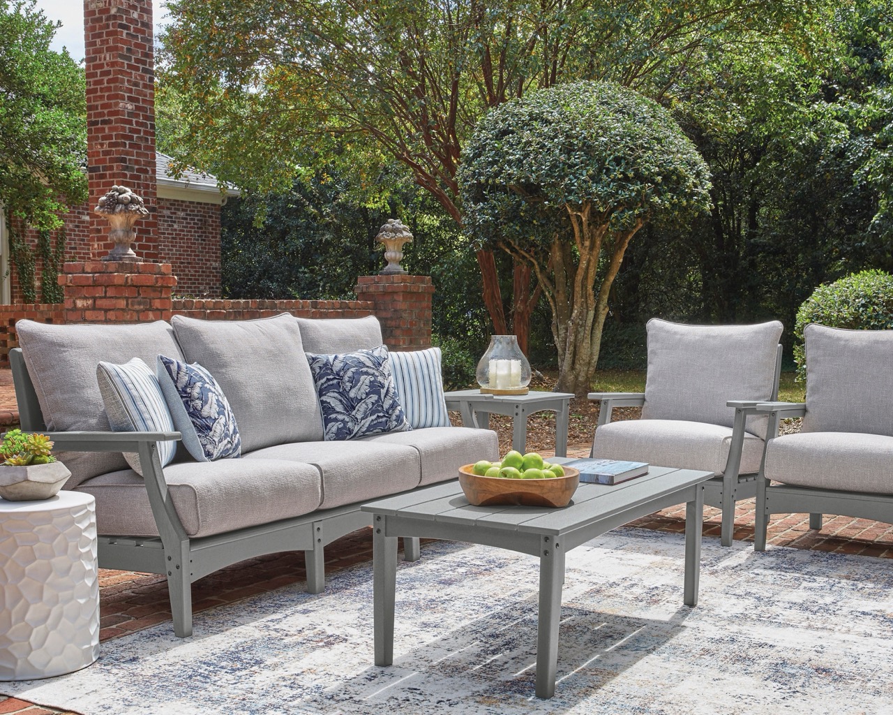 gray outdoor furniture set with two accent chairs, a sofa, and a coffee table over a rug