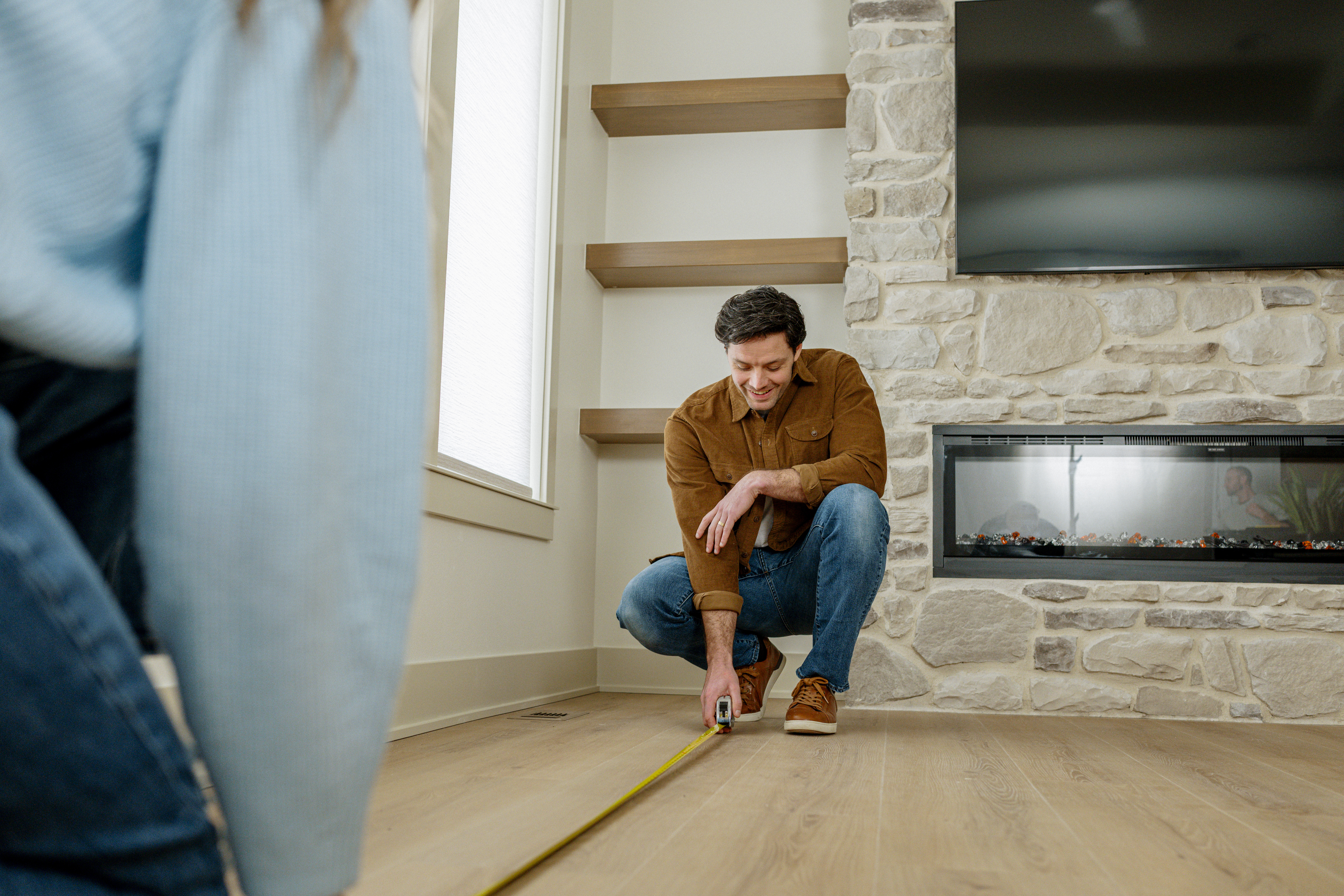 A couple measuring and empty living space with TV over firepalce