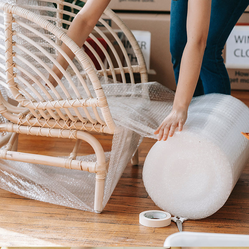 woman wrapping rattan chair in bubblewrap