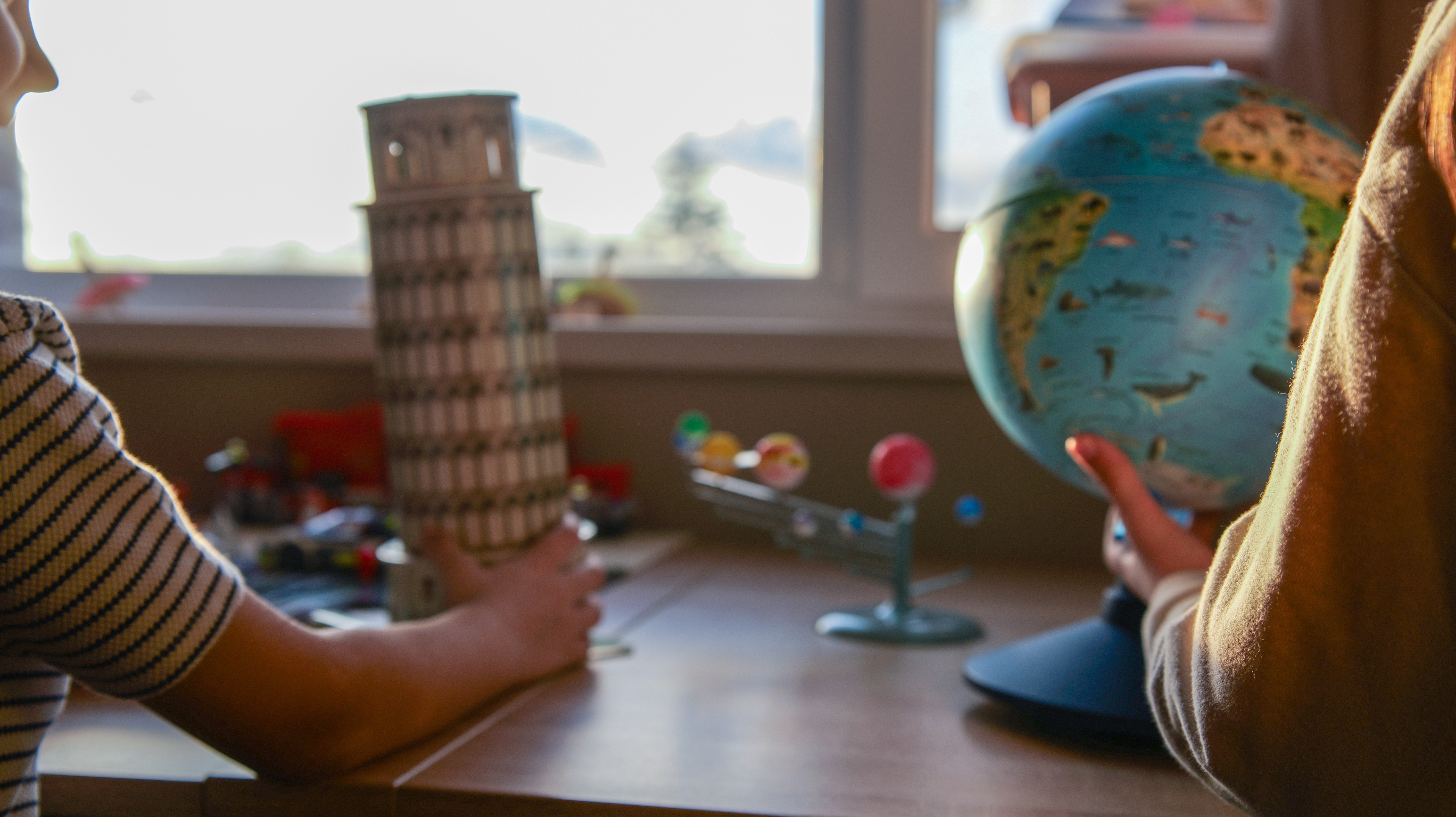 Kids hand at a learning table with globe and architectural toy