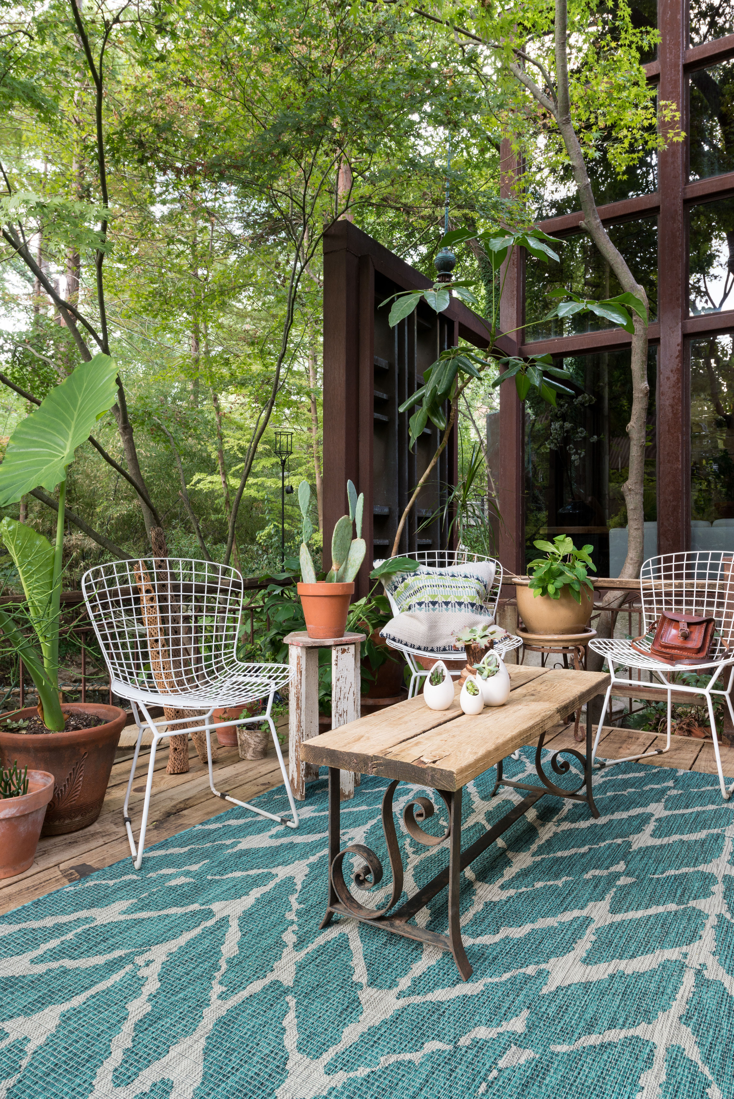 Blue-green outdoor rug with wired seating and lush green trees