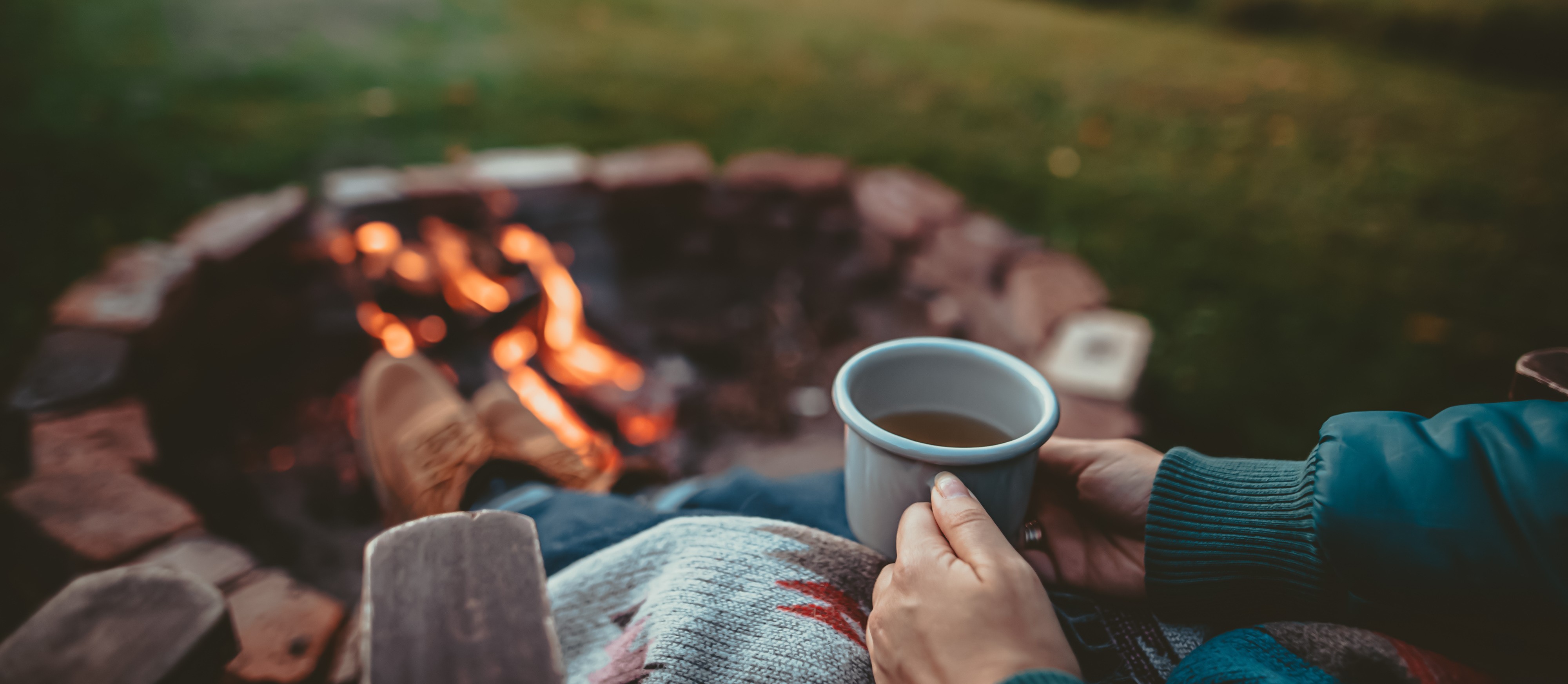 Foot resting on firepit with coffee in hands