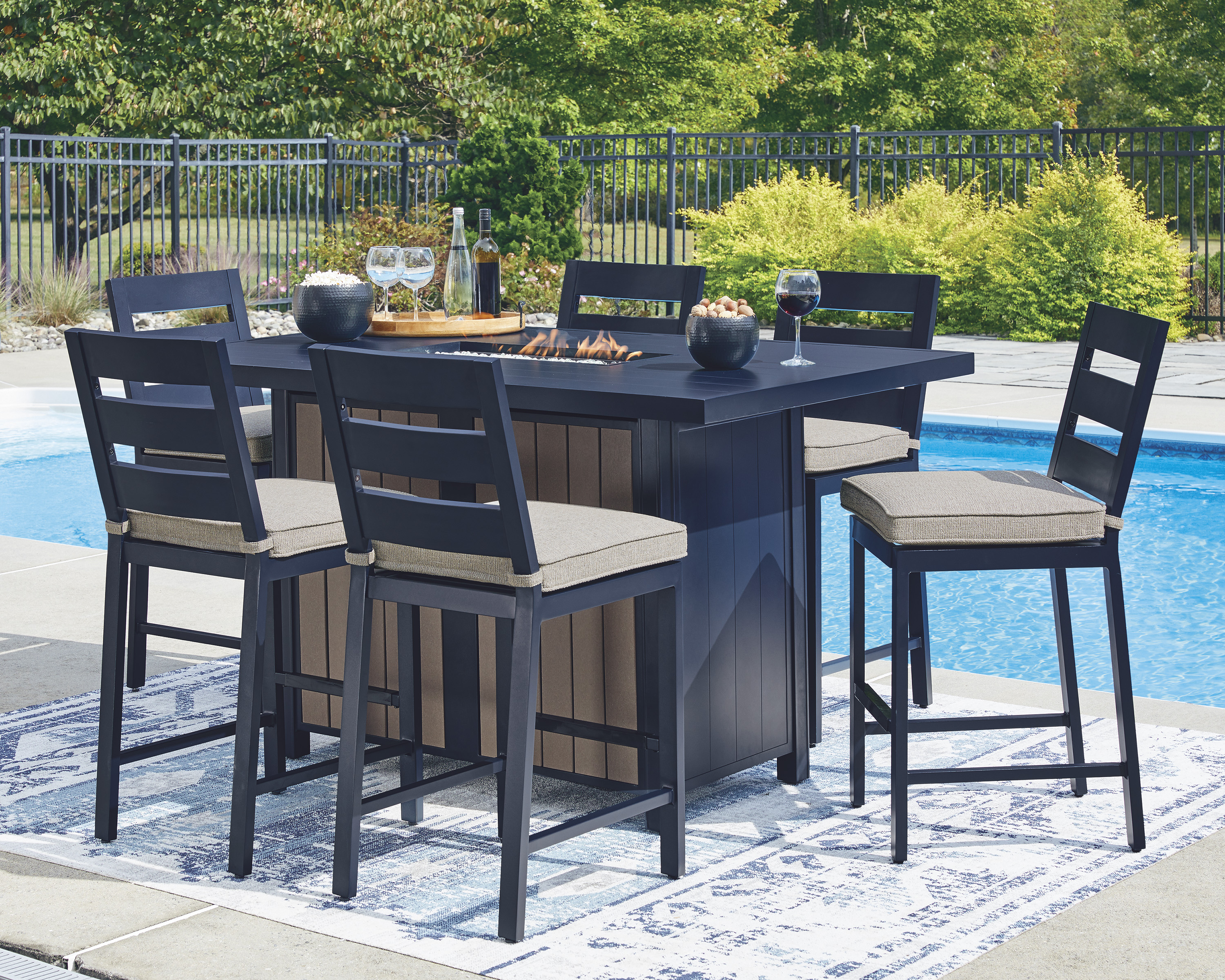 Outdoor dining set with built in firepit on outdoor rug and pool in the background