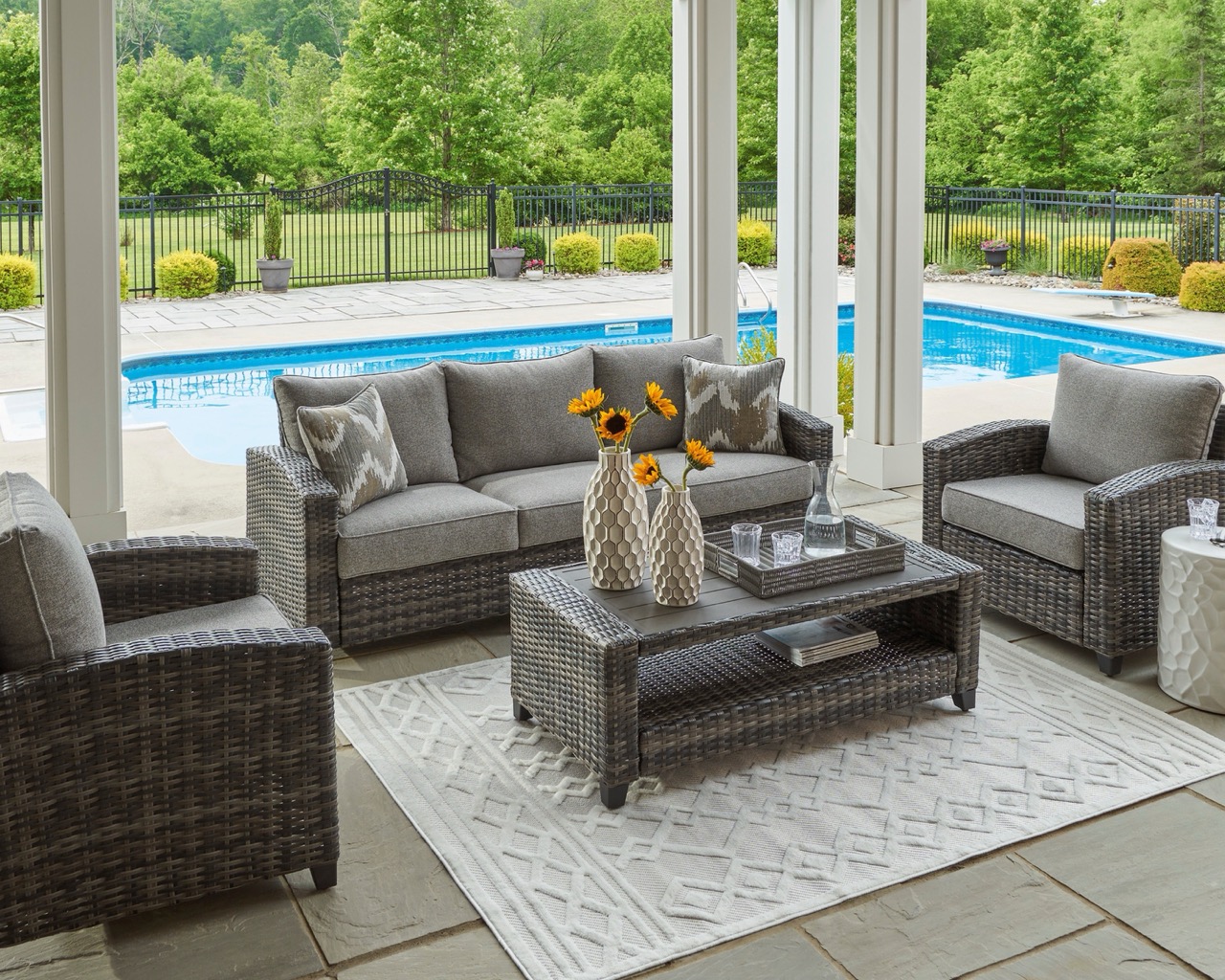 gray outdoor furniture set with a sofa, two accent chairs, and a coffee table near a pool
