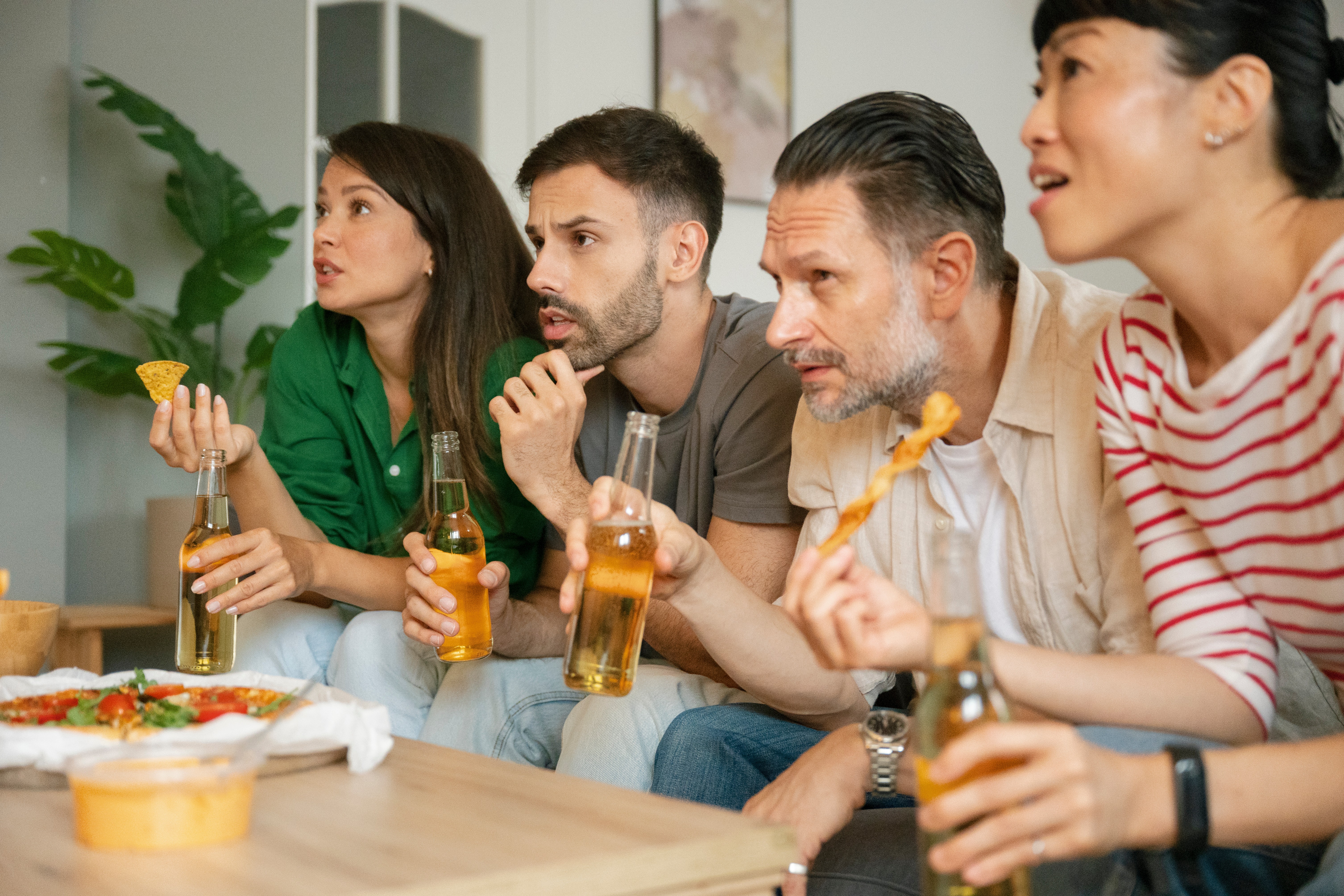 two couples enjoying food and beverage on top of coffee table while sitting on a sofa