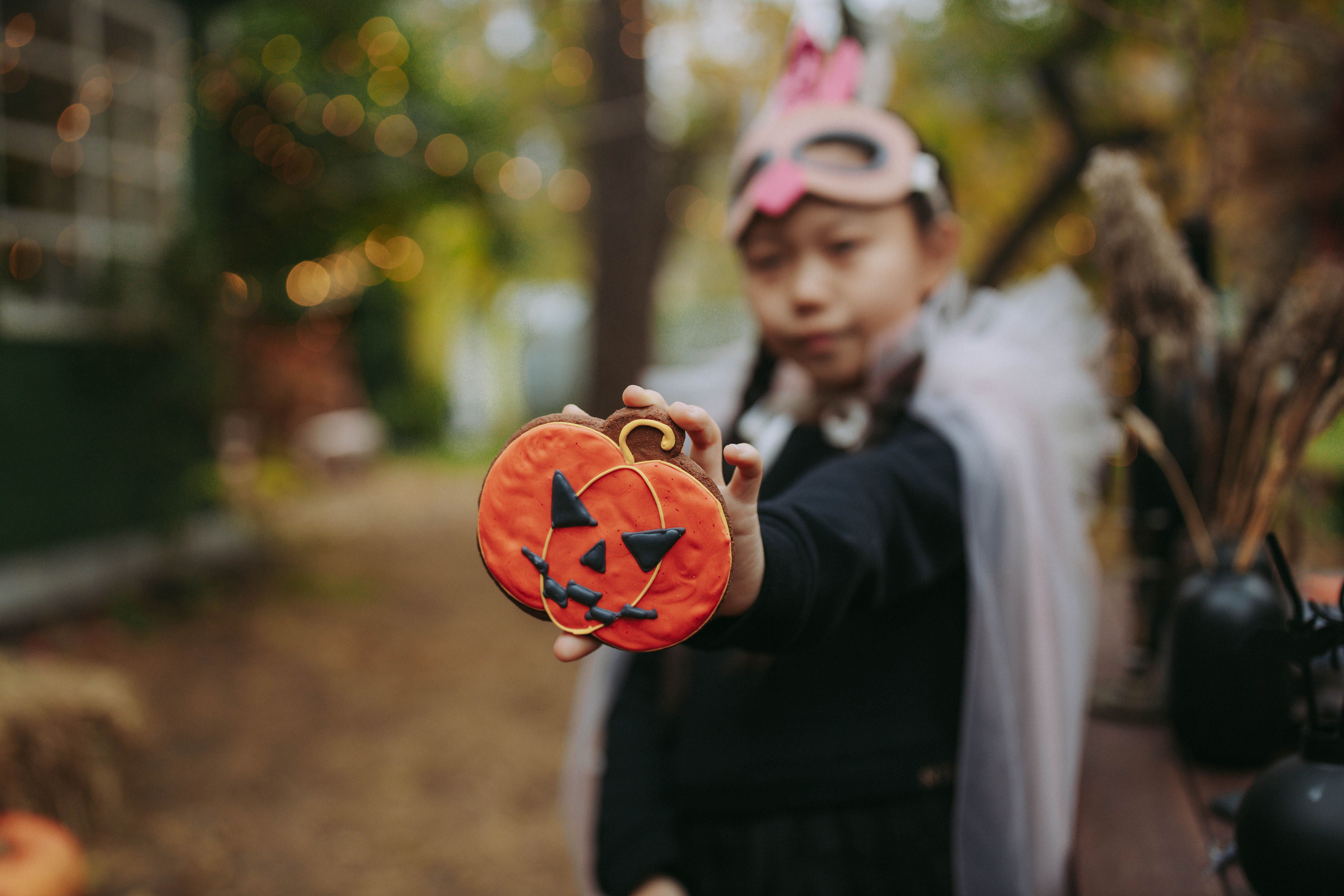 girl in black halloween costume showing off iced pumpkin cookie