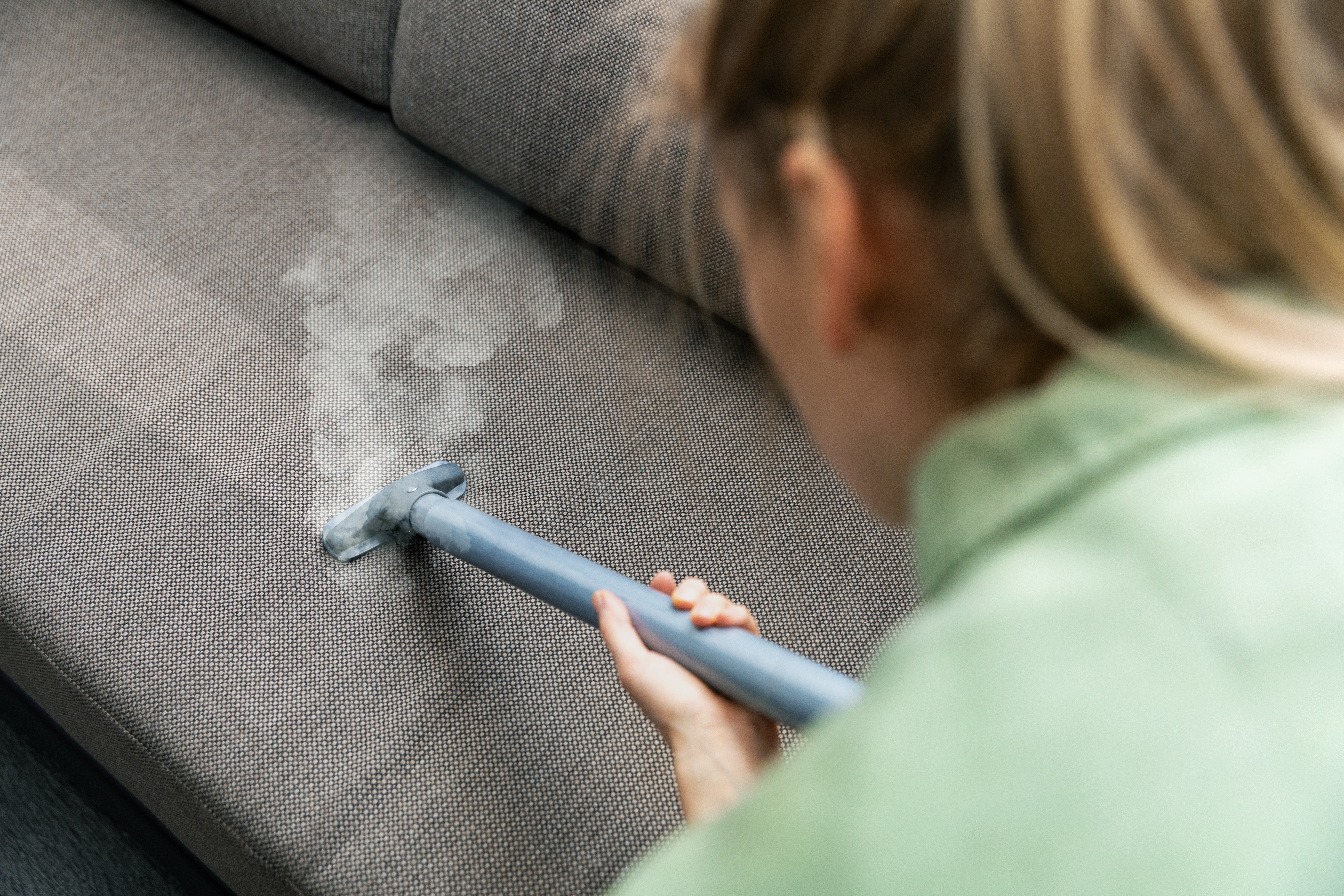 Lady vacuuming gray couch