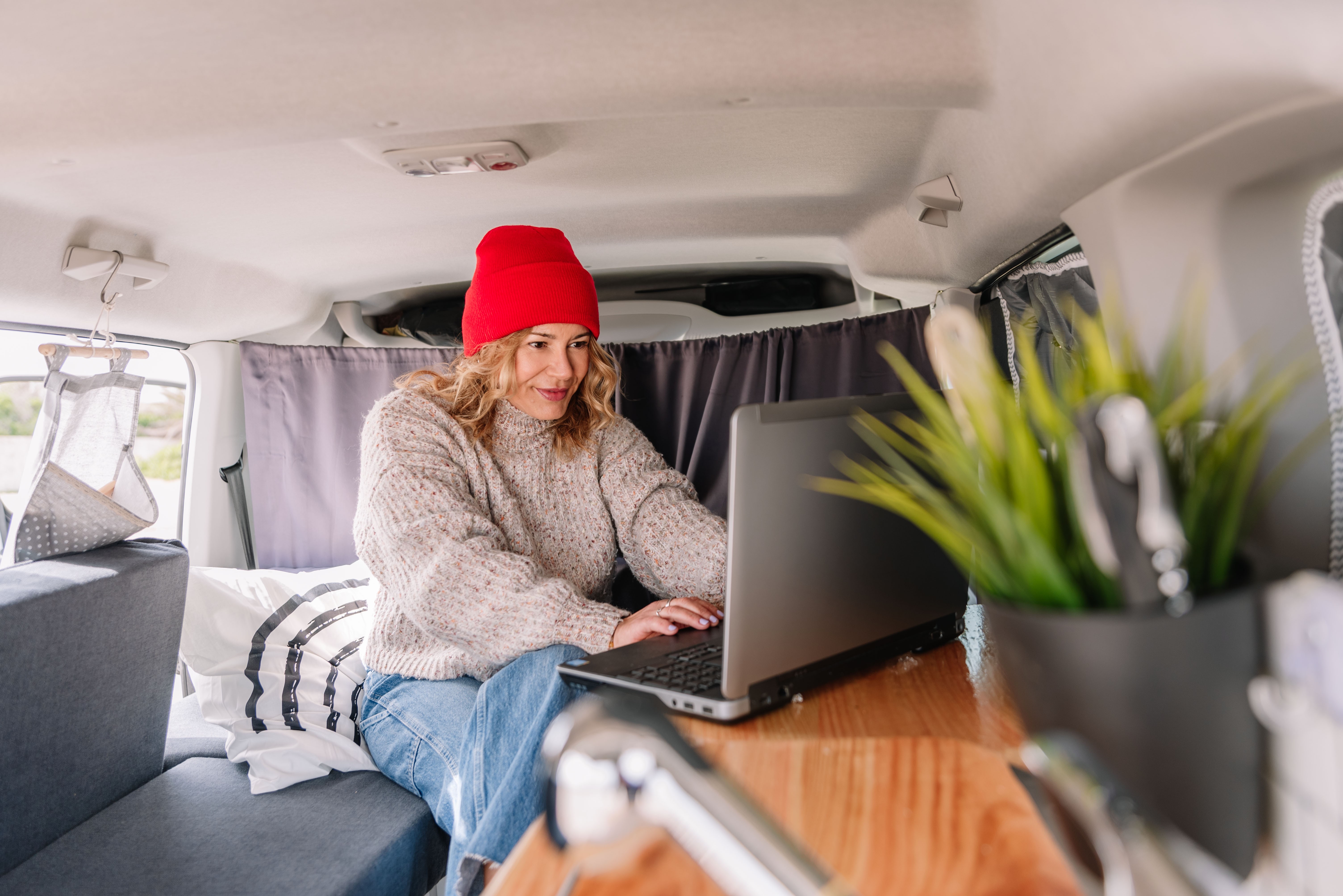 Woman with red knit hat working on laptop in her van